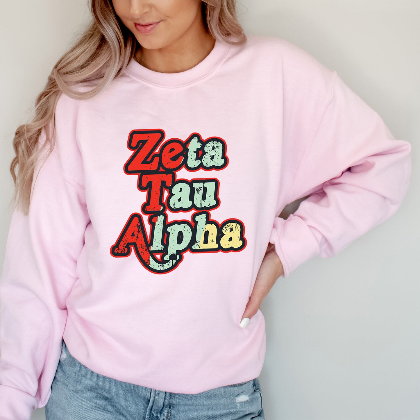 a woman wearing a pink sweatshirt that says zeta tau alpha
