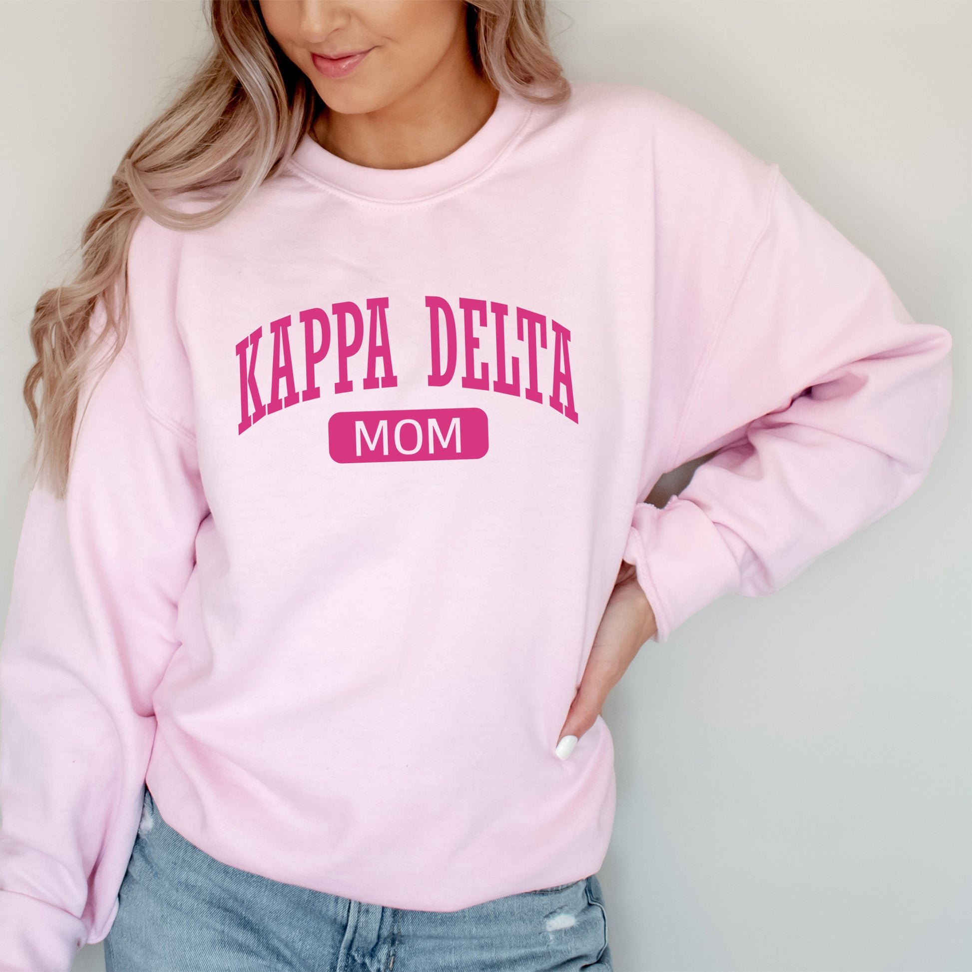 a woman wearing a pink sweatshirt that says kapa delta mom