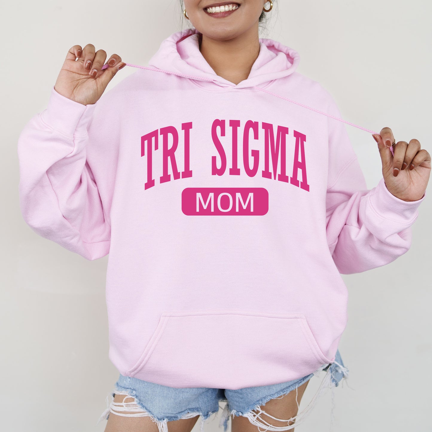 a woman wearing a pink hoodie that says tri sigma mom