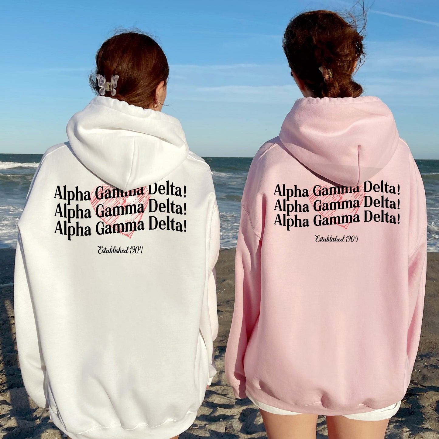 two women wearing pink and white hoodies on the beach