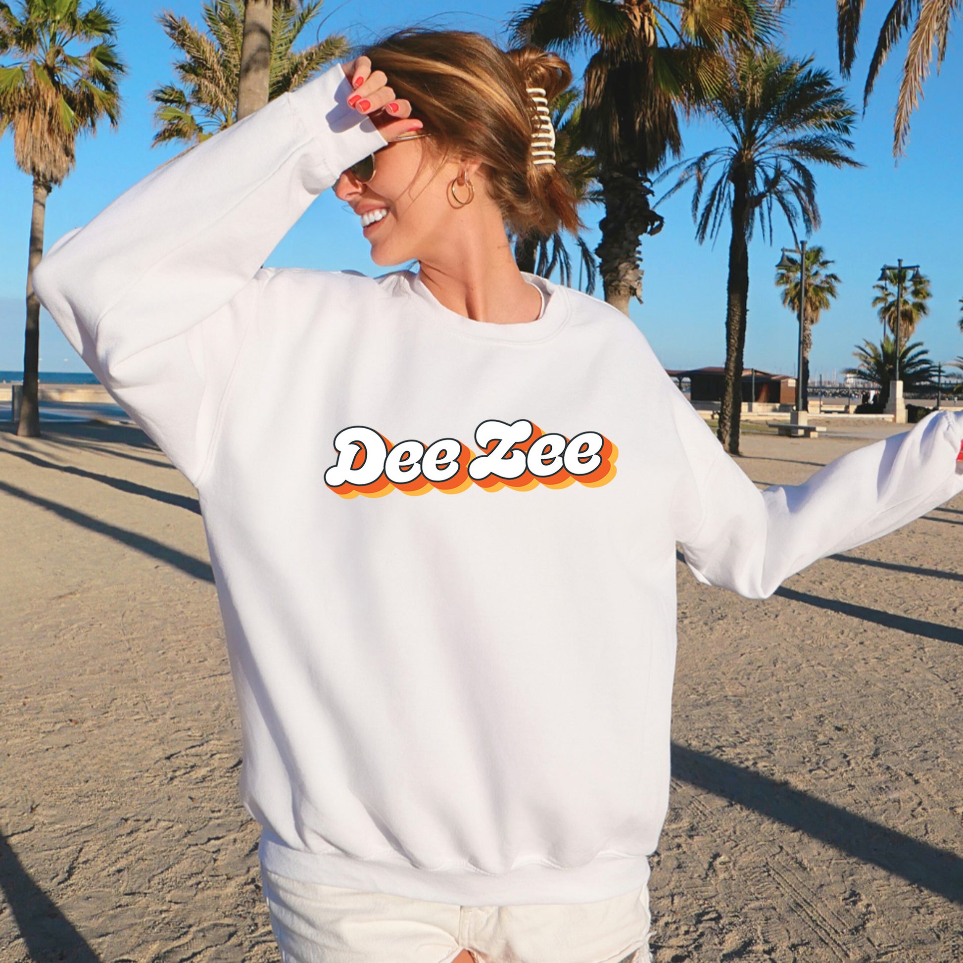 a woman standing on a beach wearing a white sweatshirt