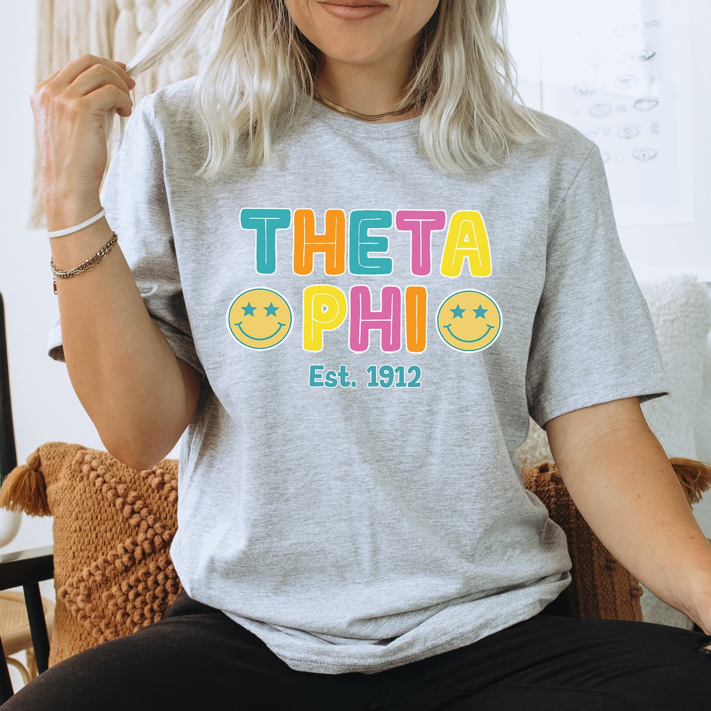 a woman sitting on a chair wearing a t - shirt that says theta phi