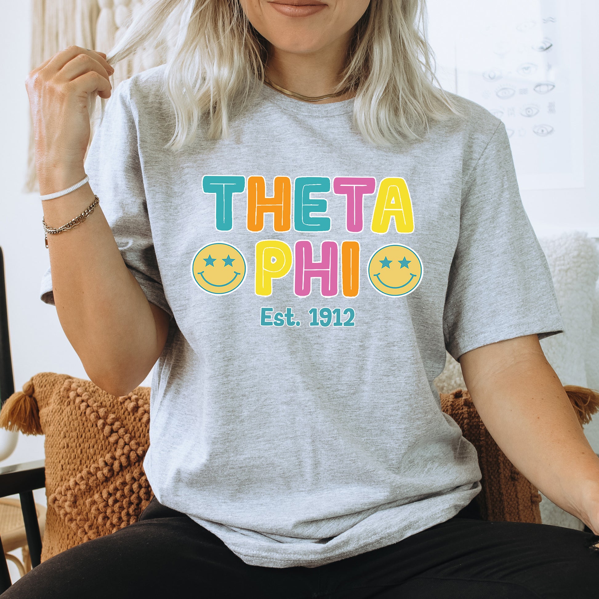 a woman sitting on a chair wearing a t - shirt that says theta phi