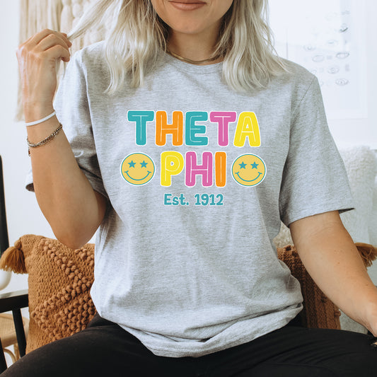 a woman sitting on a chair wearing a t - shirt that says theta phi