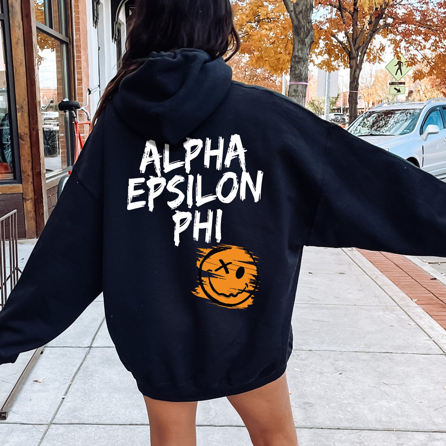 a woman walking down a sidewalk wearing a black hoodie