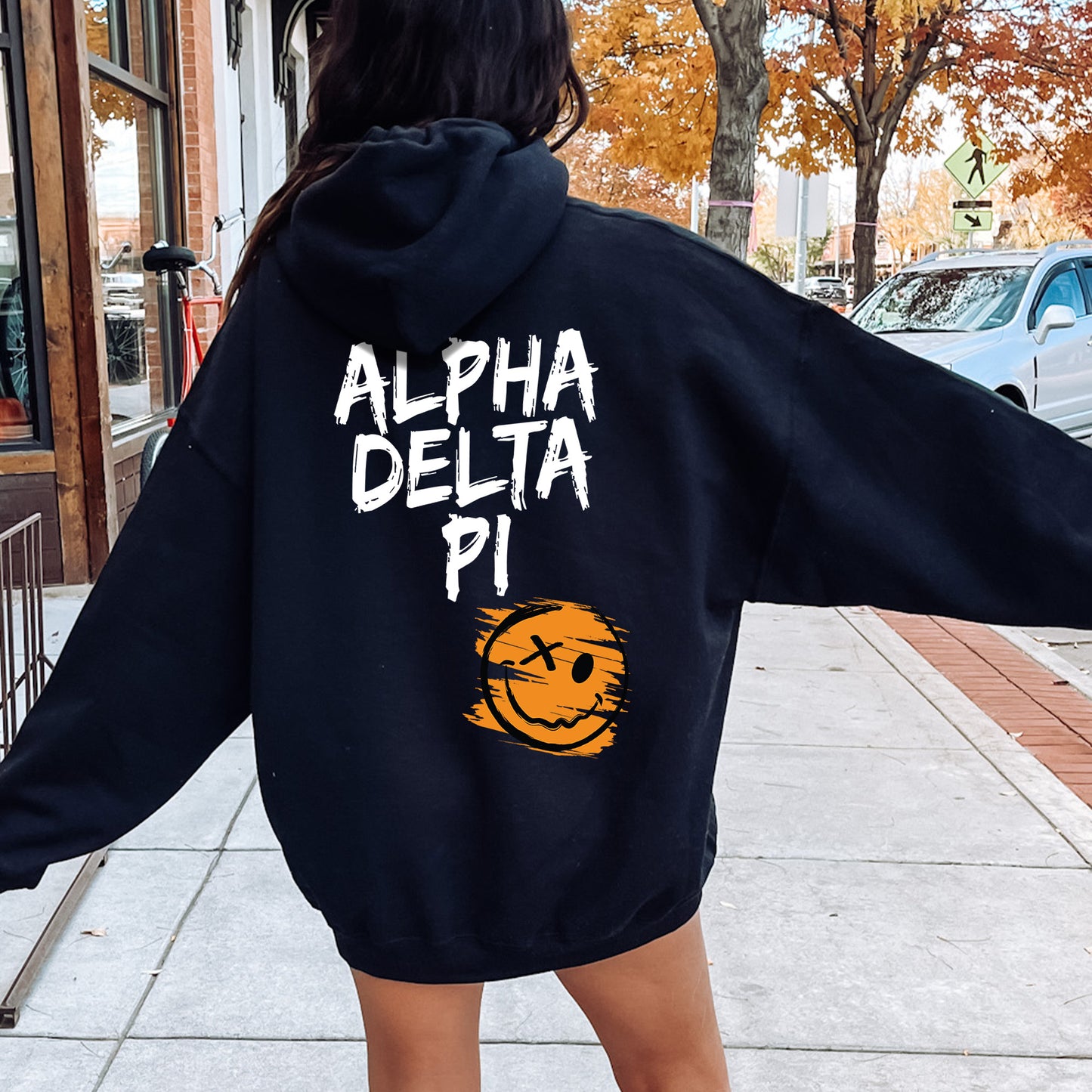 a woman walking down a sidewalk wearing a black hoodie