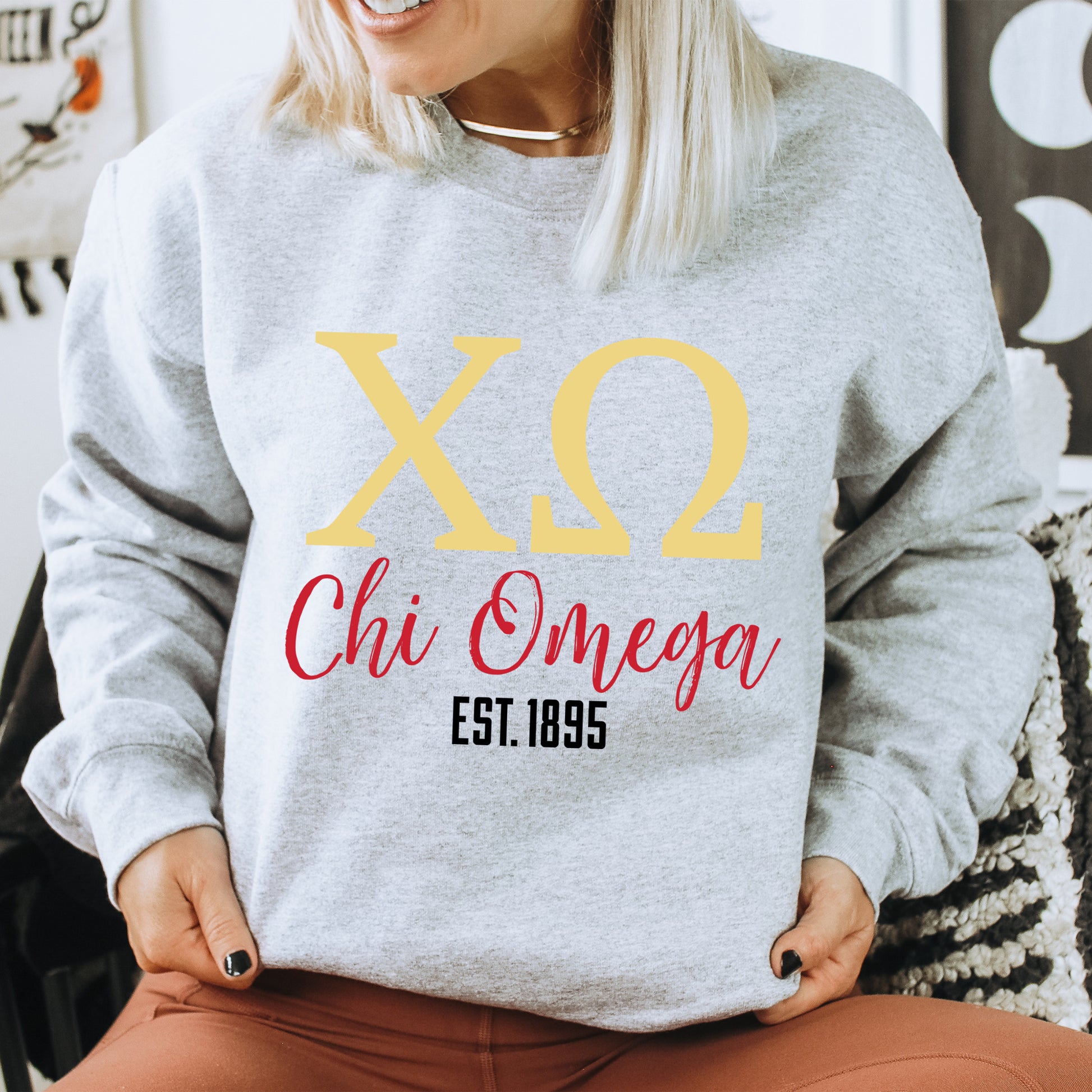 a woman sitting on a chair wearing a sweatshirt that says x2 chi omega est