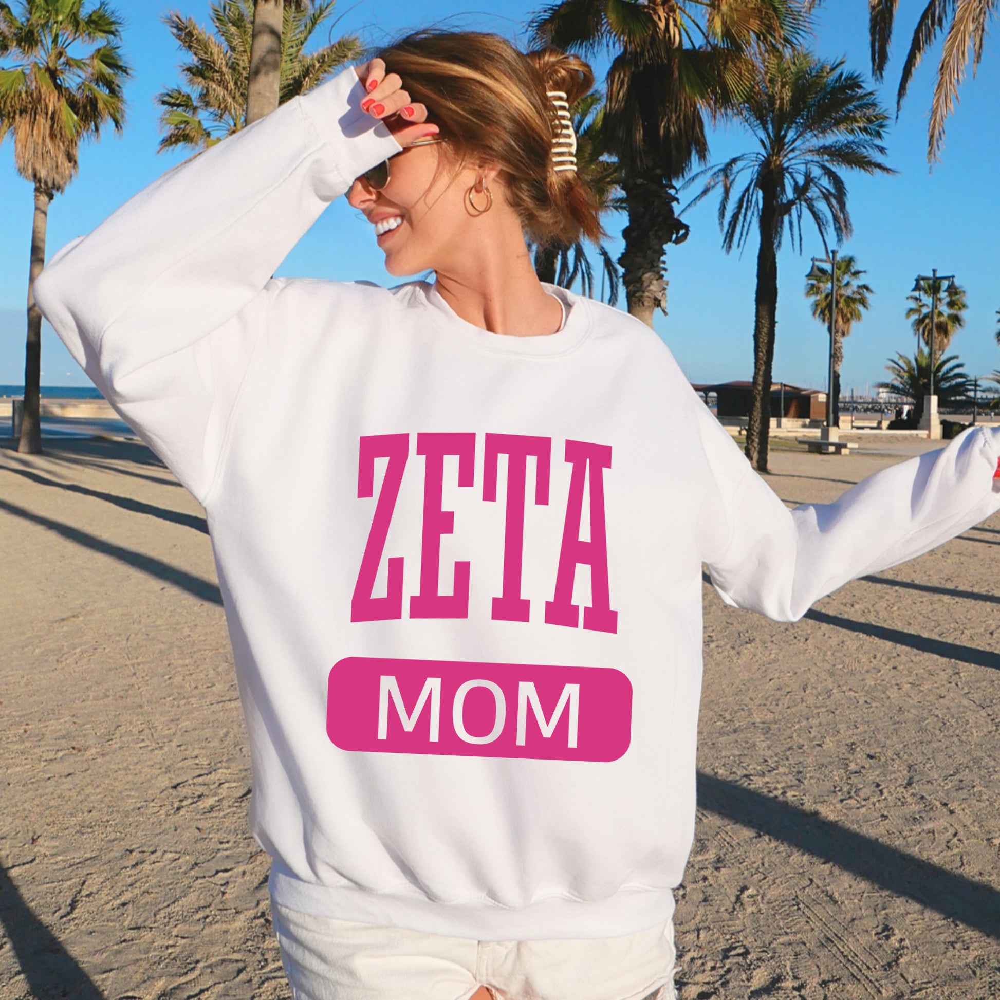 a woman standing on a beach wearing a sweatshirt that says zetta mom