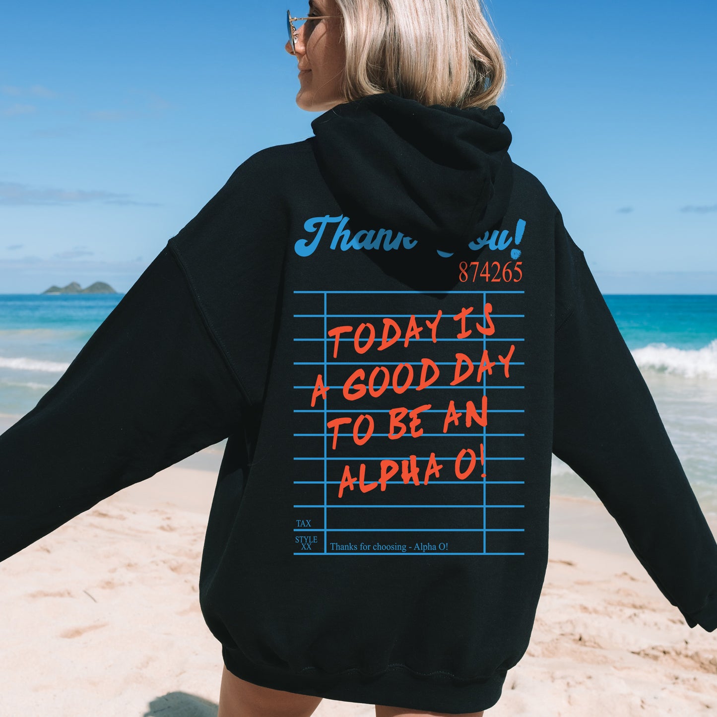 a woman standing on a beach wearing a black hoodie