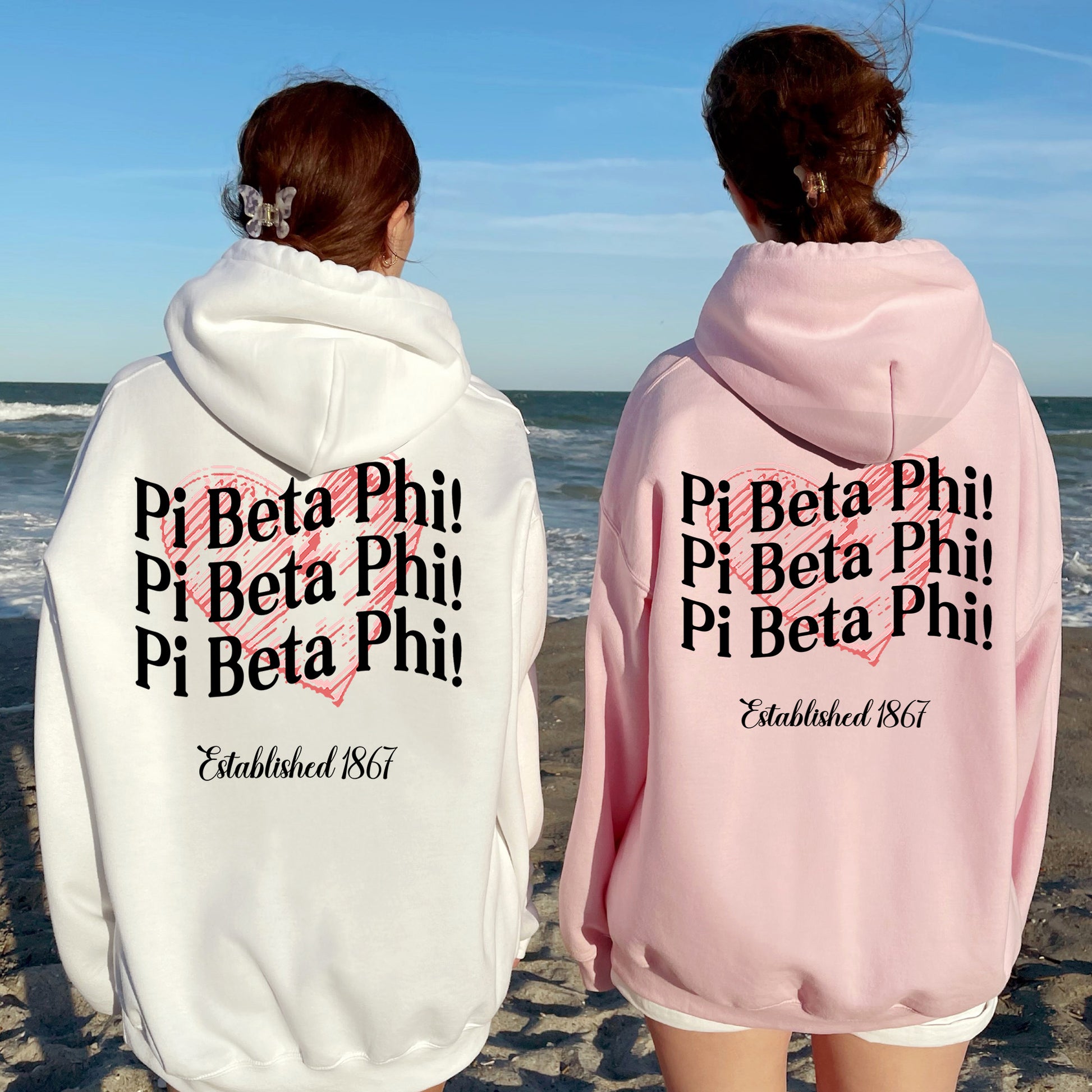 two people standing on a beach wearing matching sweatshirts
