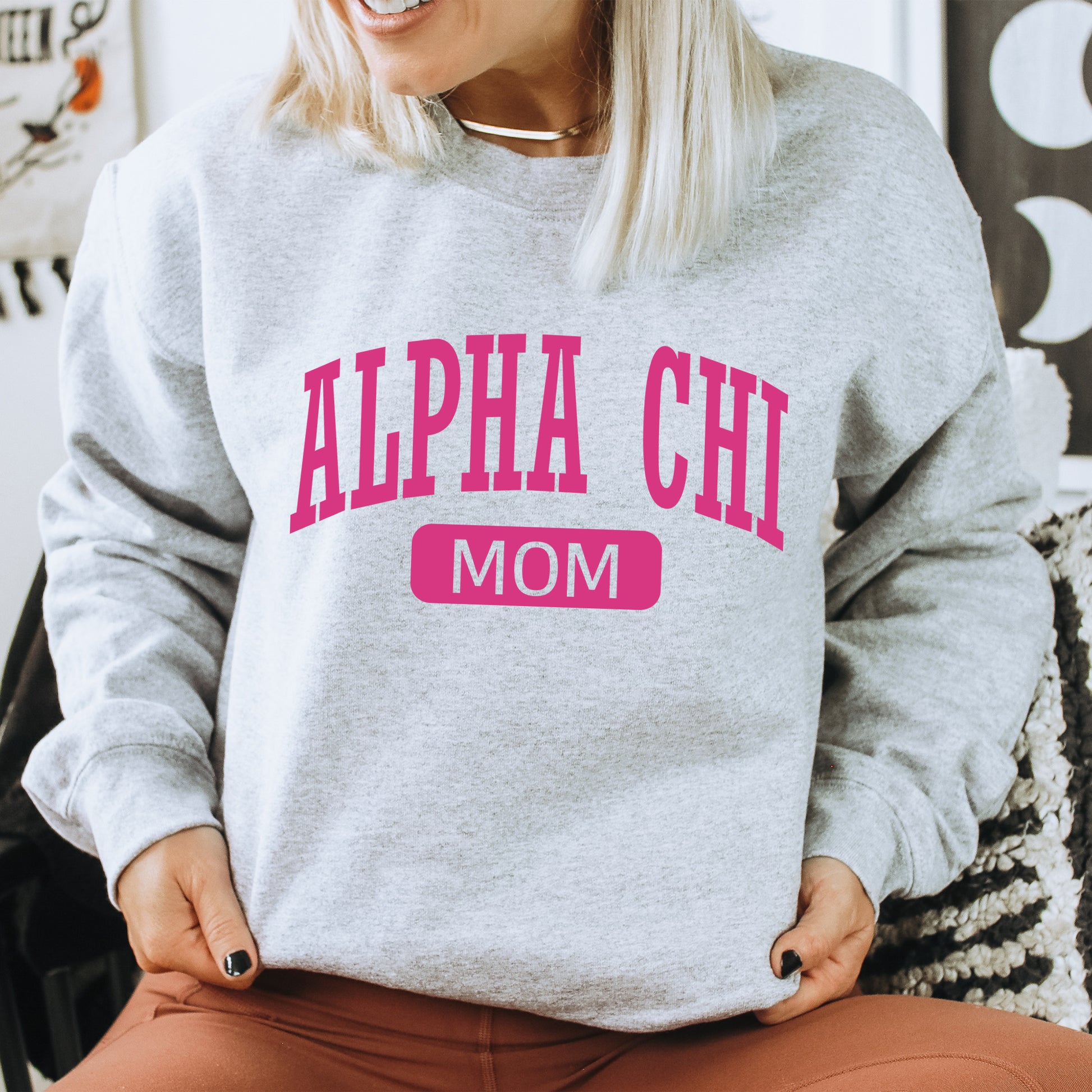 a woman sitting in a chair wearing a gray sweatshirt with pink letters
