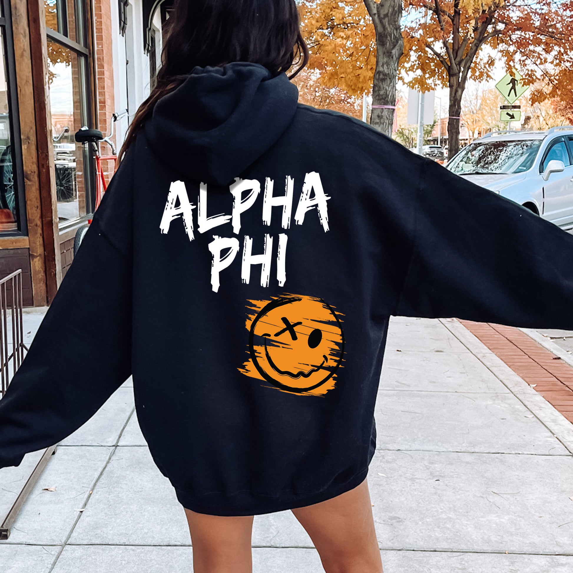 a woman walking down a sidewalk wearing a black hoodie