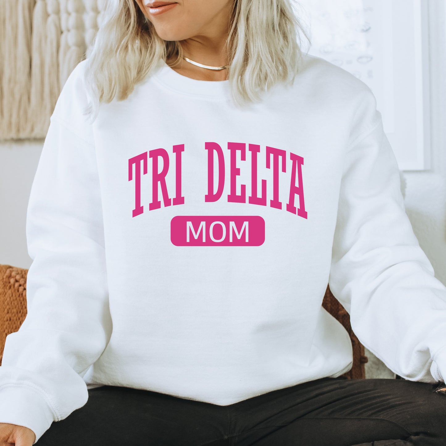 a woman sitting on a chair wearing a sweatshirt that says tri delta mom