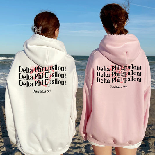 two women standing on a beach wearing matching sweatshirts