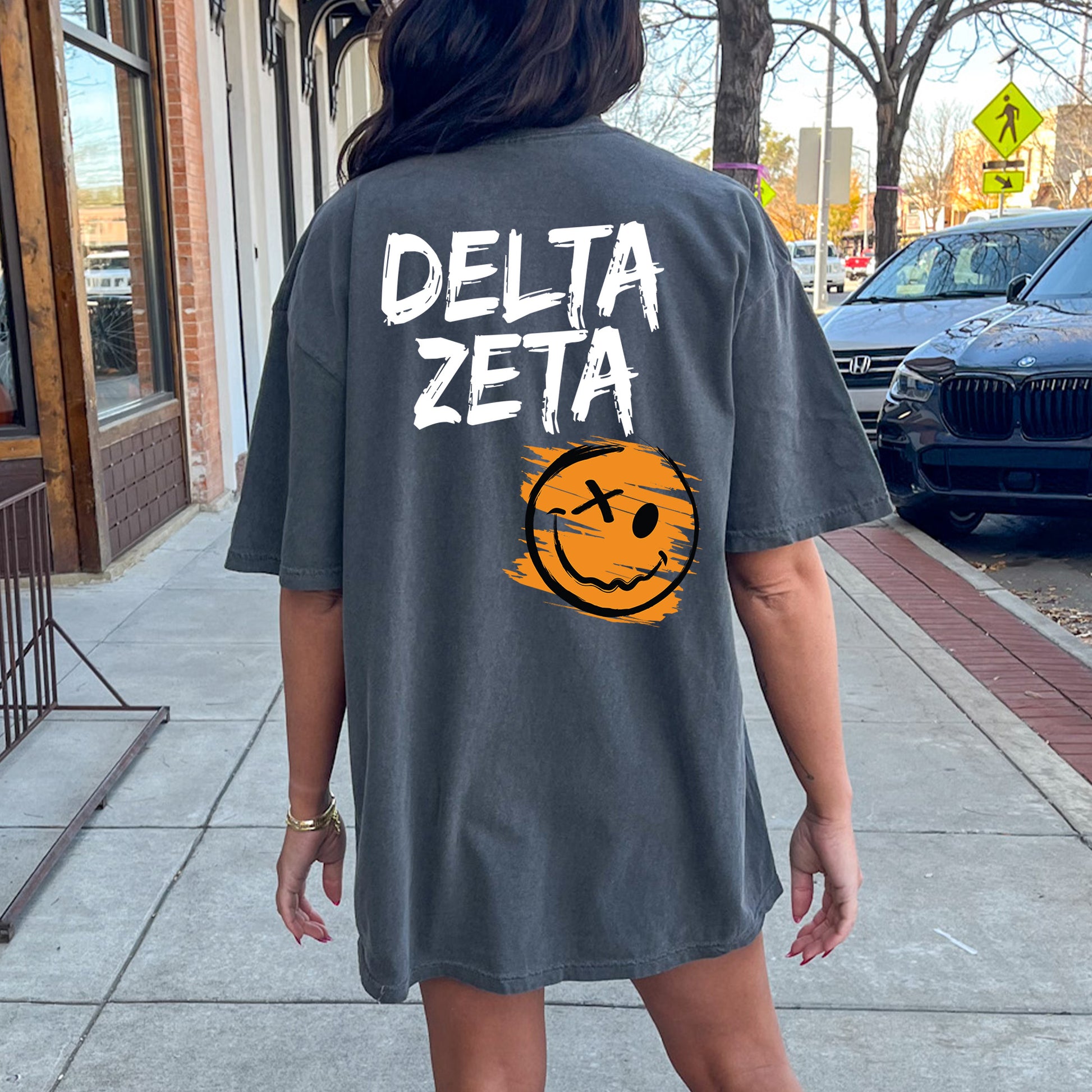 a woman walking down a sidewalk wearing a shirt that says delta zeta