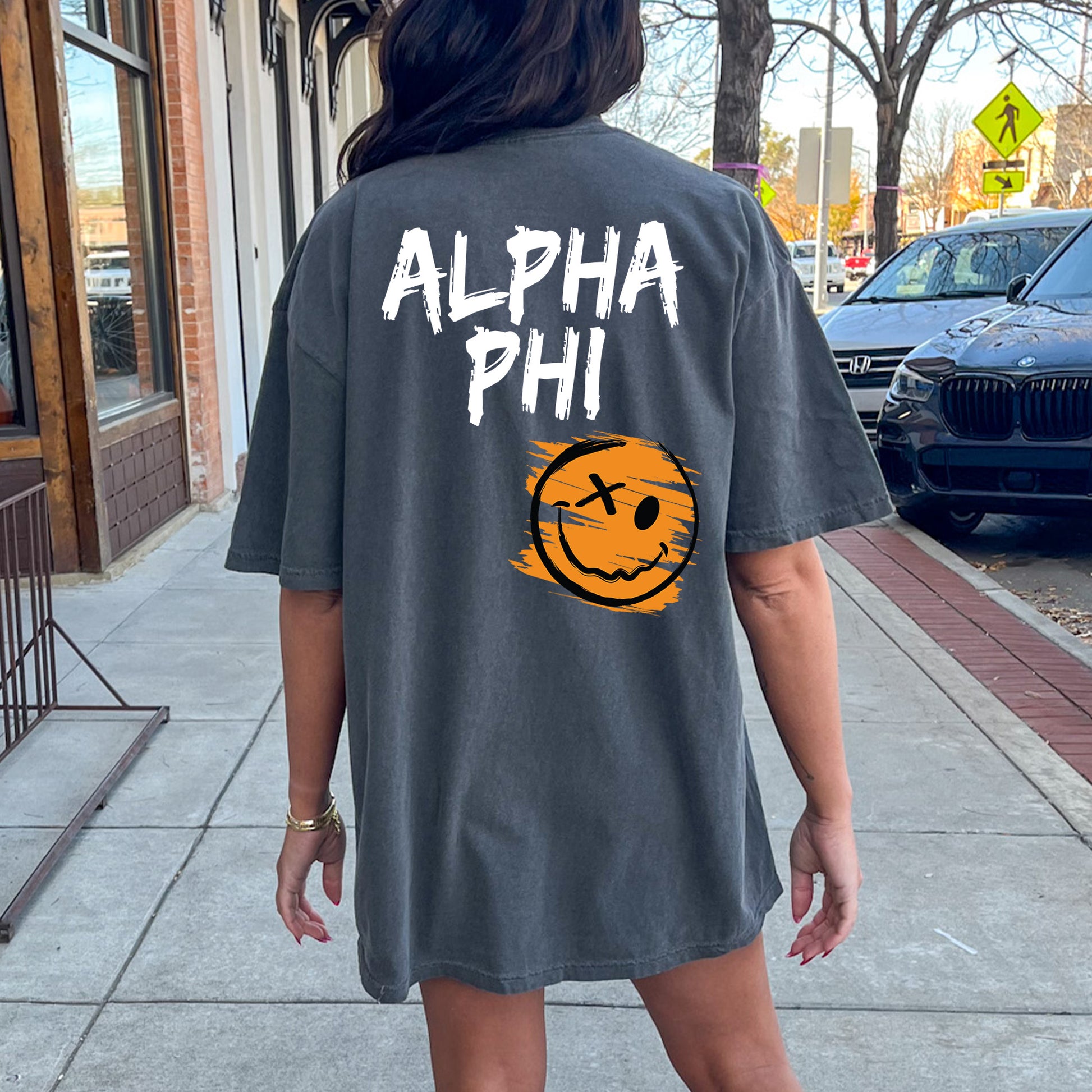 a woman walking down a sidewalk wearing a shirt with a smiley face on it