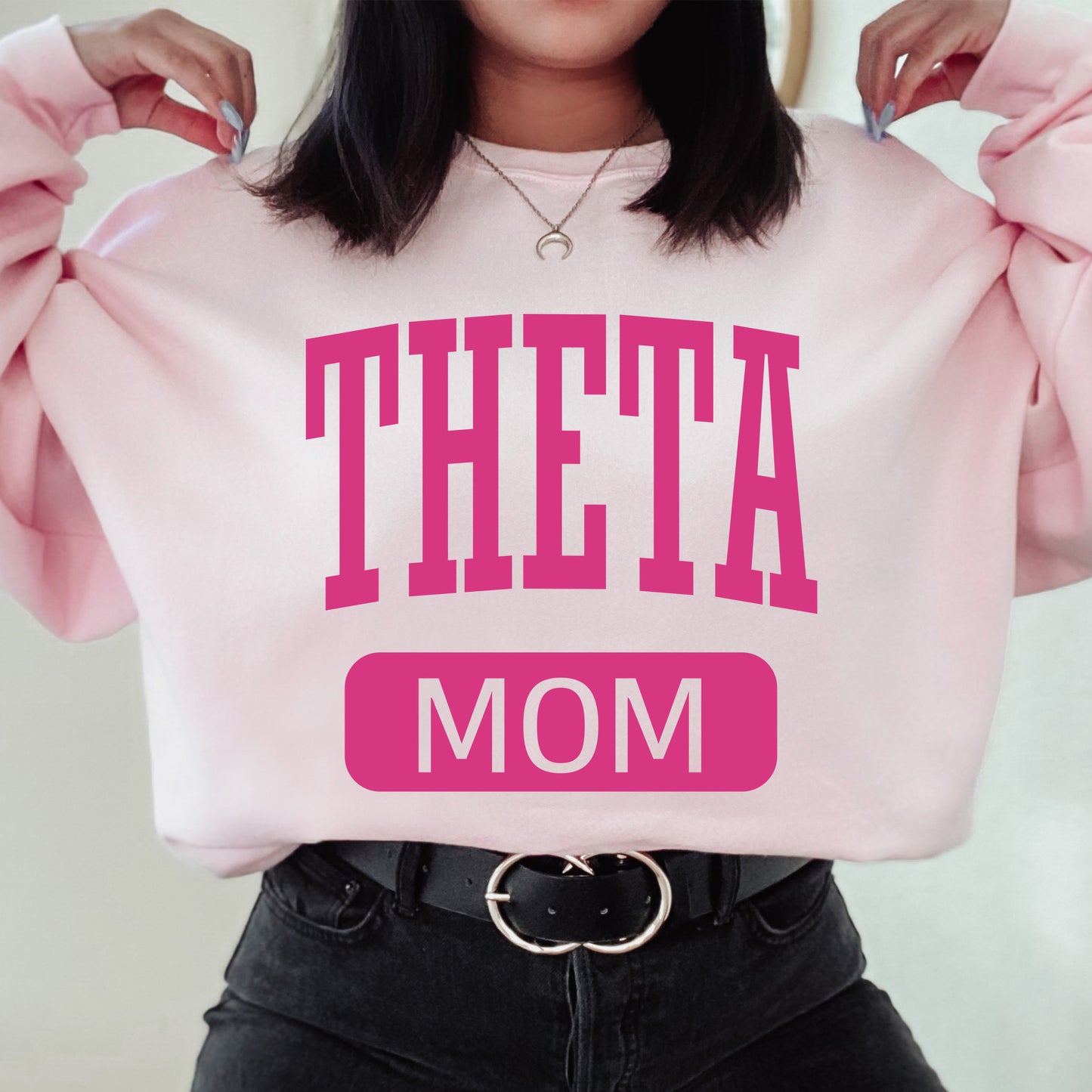 a woman holding a pink sweatshirt with the words'theta mom'on it