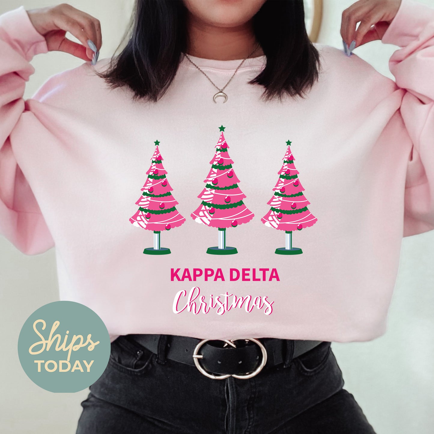 a woman holding up a pink sweatshirt with christmas trees on it