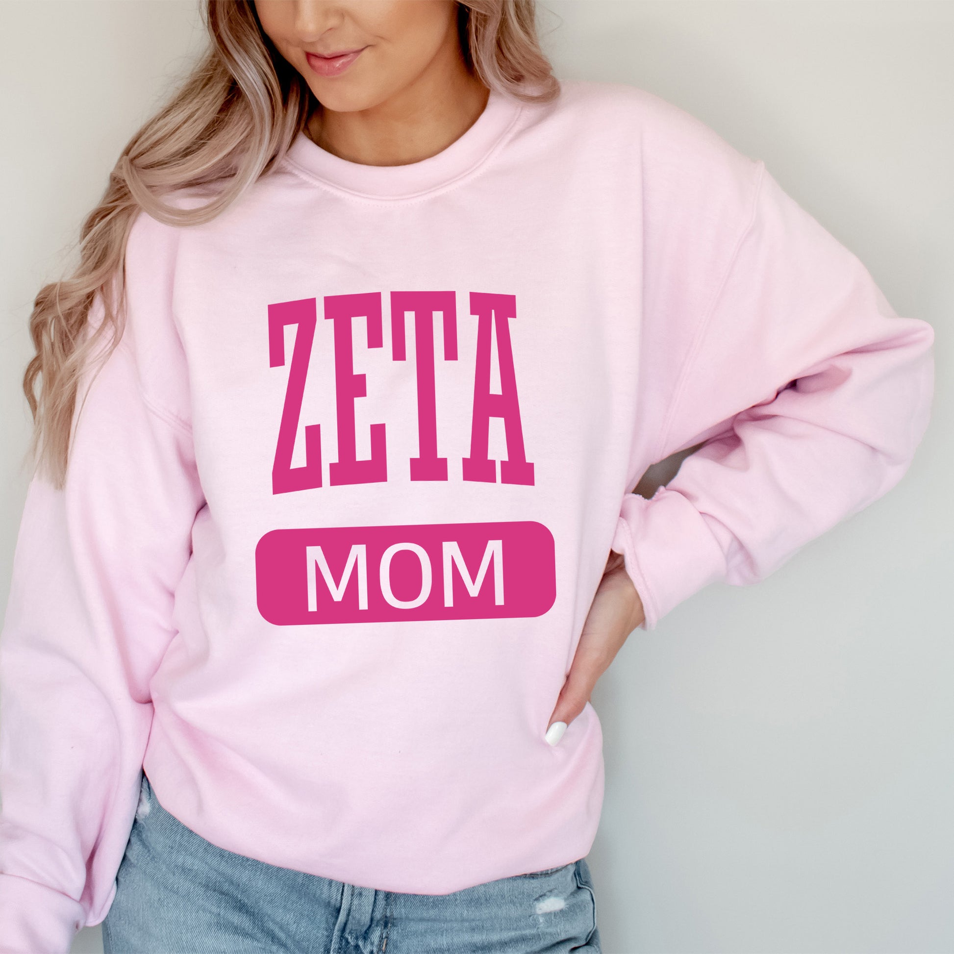 a woman wearing a pink sweatshirt that says zeta mom