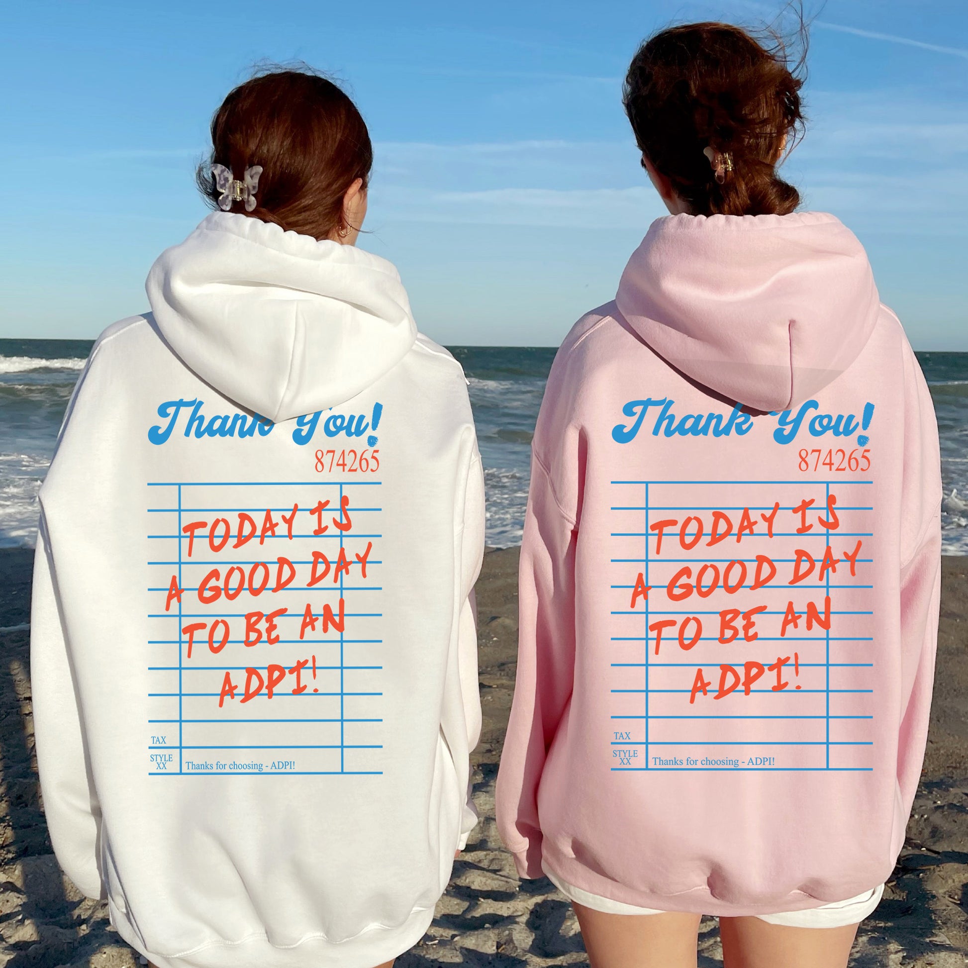 two people standing on a beach wearing matching sweatshirts