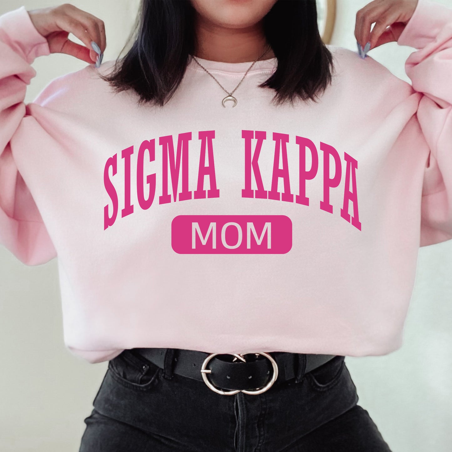 a woman wearing a pink sweatshirt that says stigmaa kappa mom