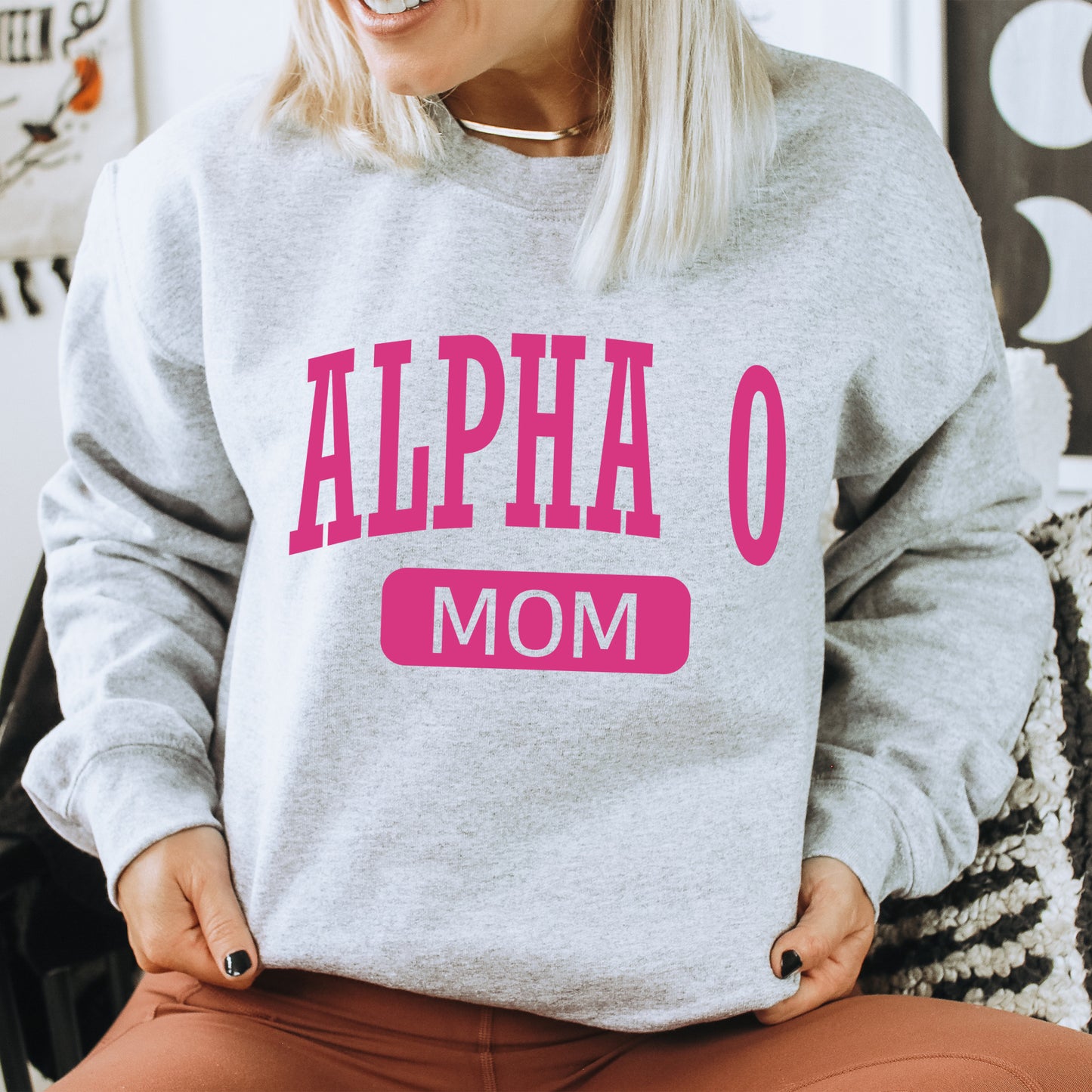 a woman sitting on a chair wearing a gray sweatshirt with pink letters