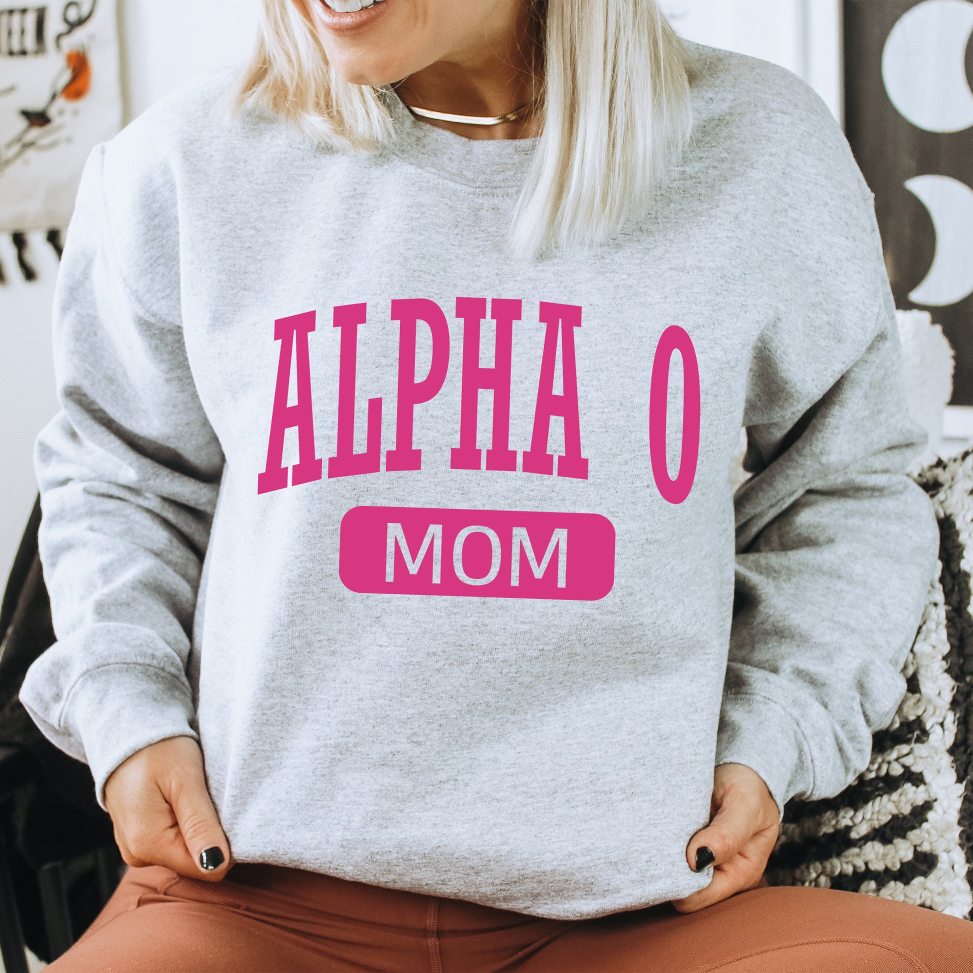 a woman sitting on a chair wearing a gray sweatshirt with pink letters