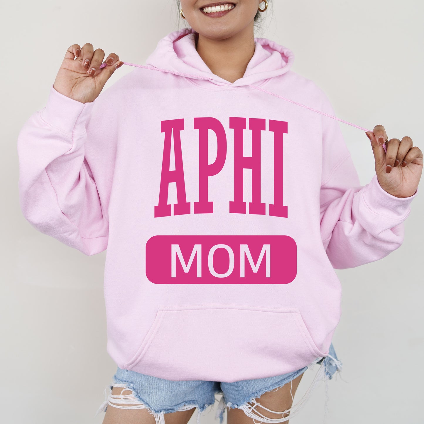 a woman wearing a pink hoodie that says aphi mom