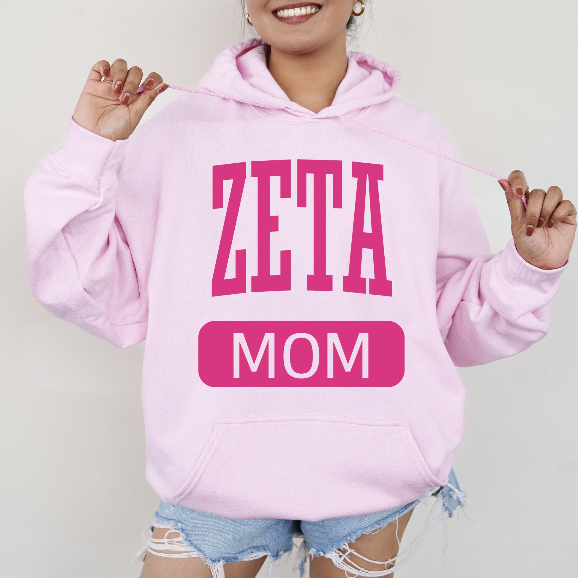 a woman wearing a pink hoodie that says zeta mom