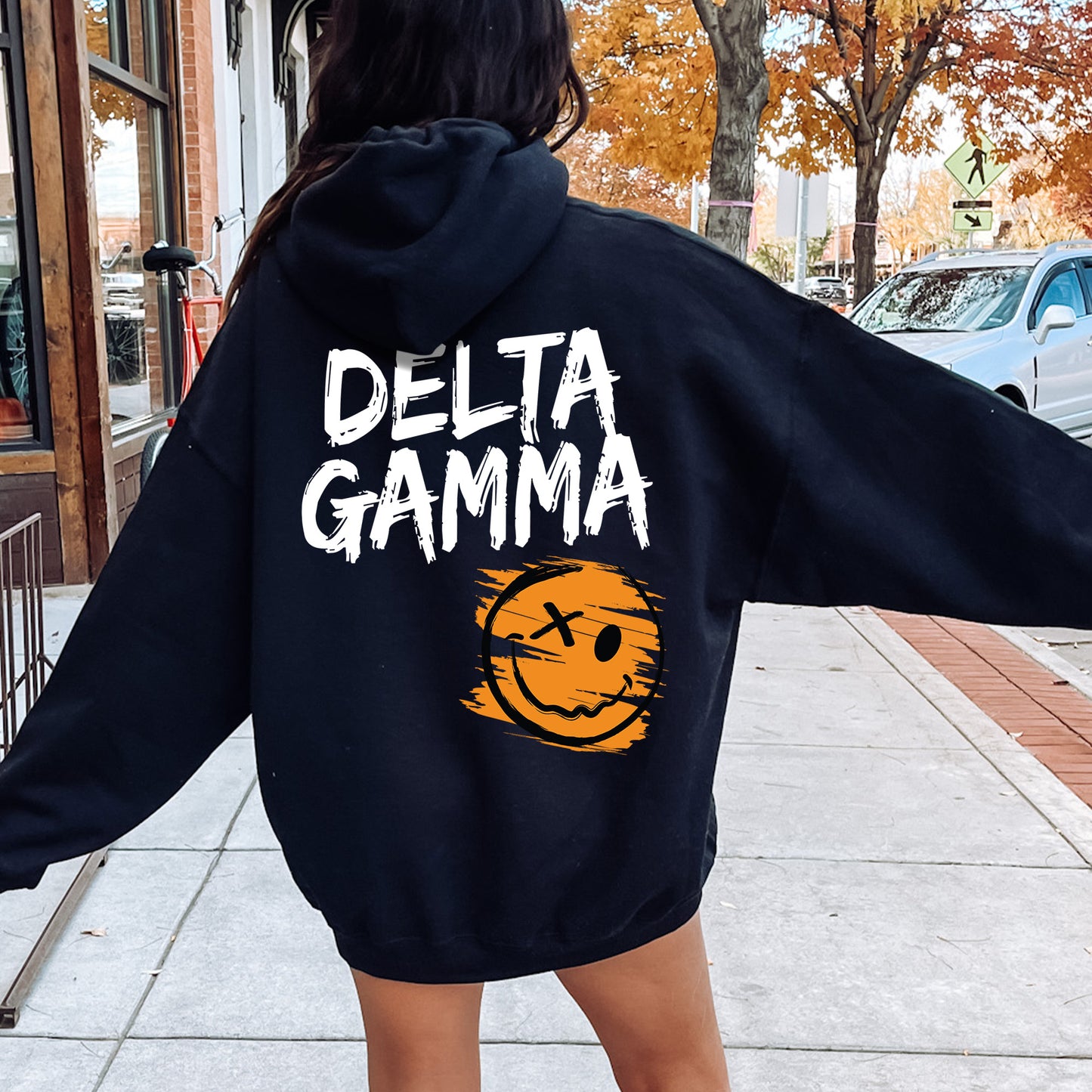 a woman walking down a sidewalk wearing a black hoodie