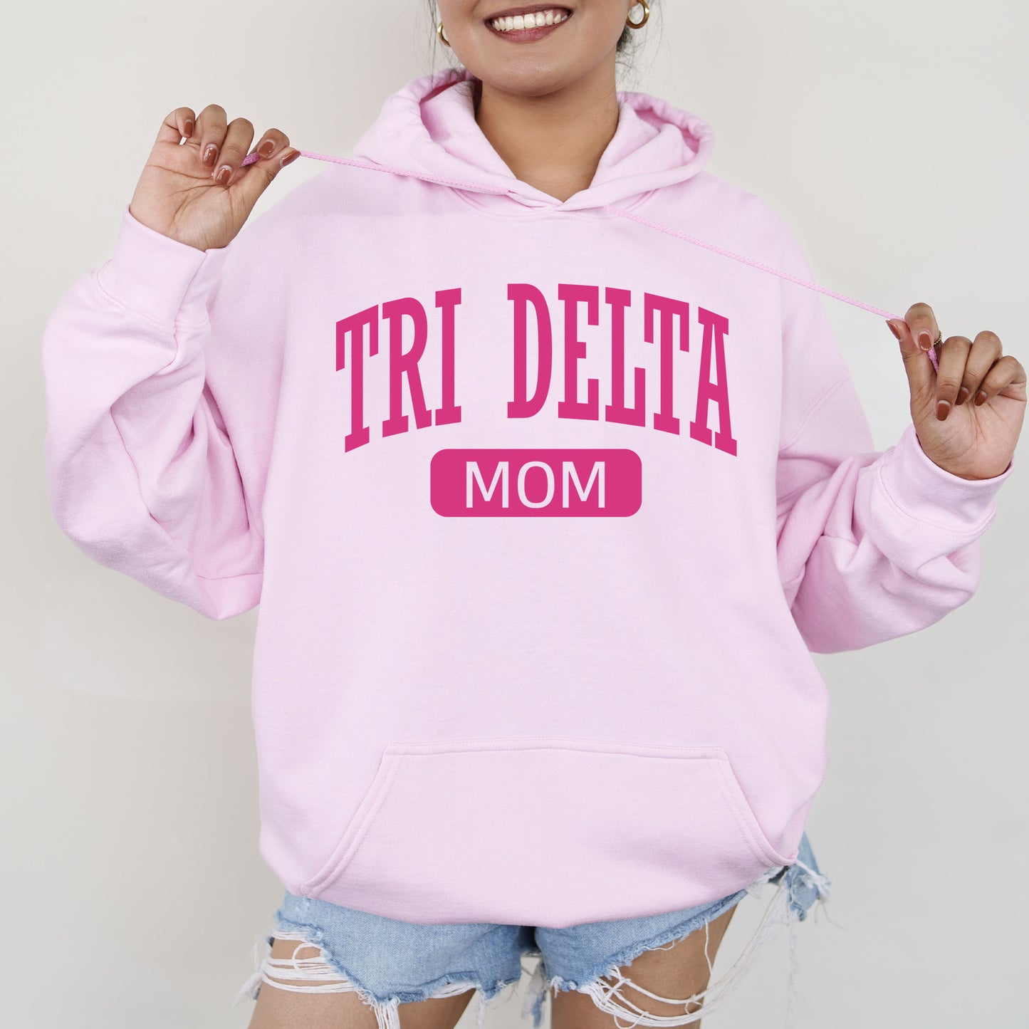 a woman wearing a pink hoodie that says tri delta mom
