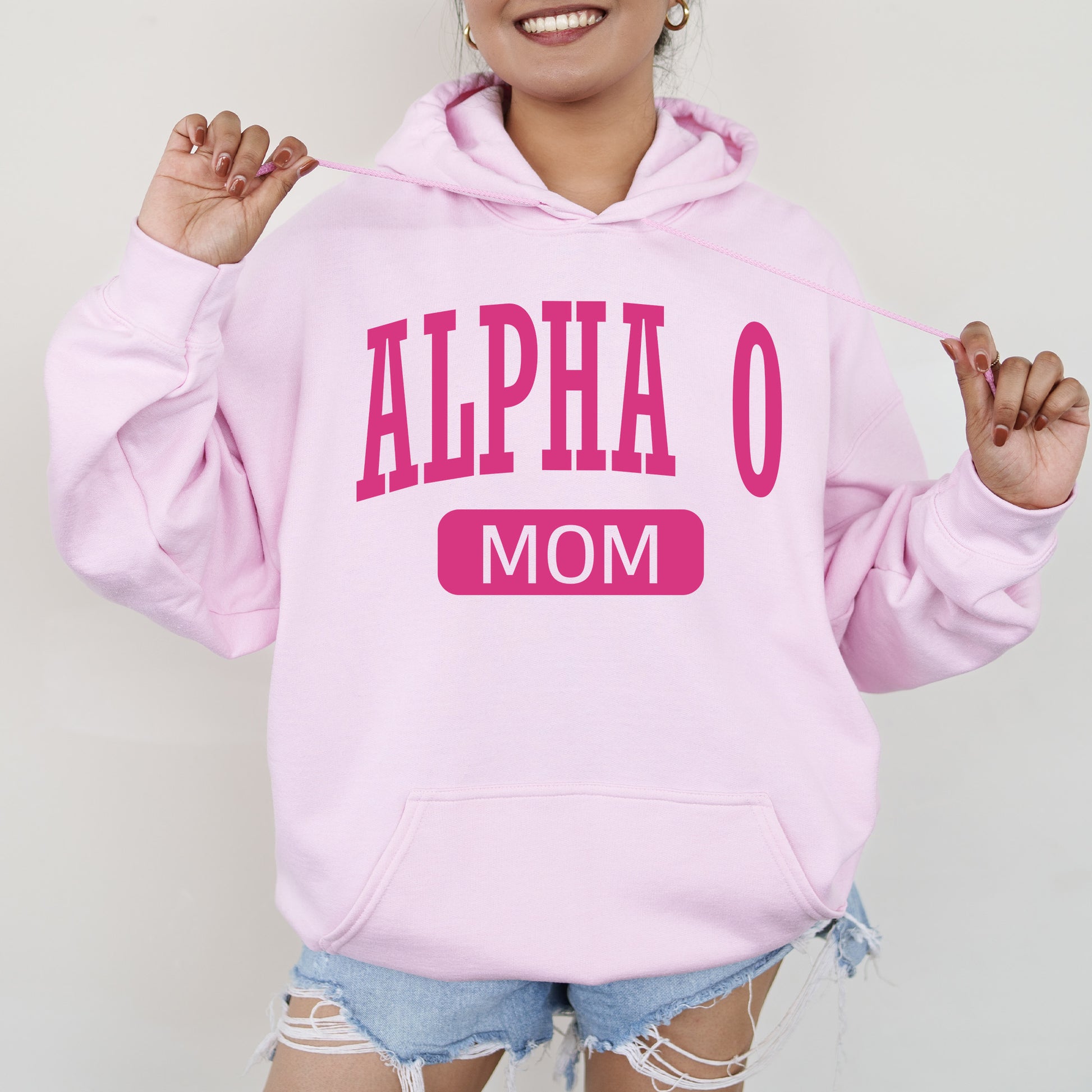 a woman wearing a pink hoodie that says,'alpha o mom '