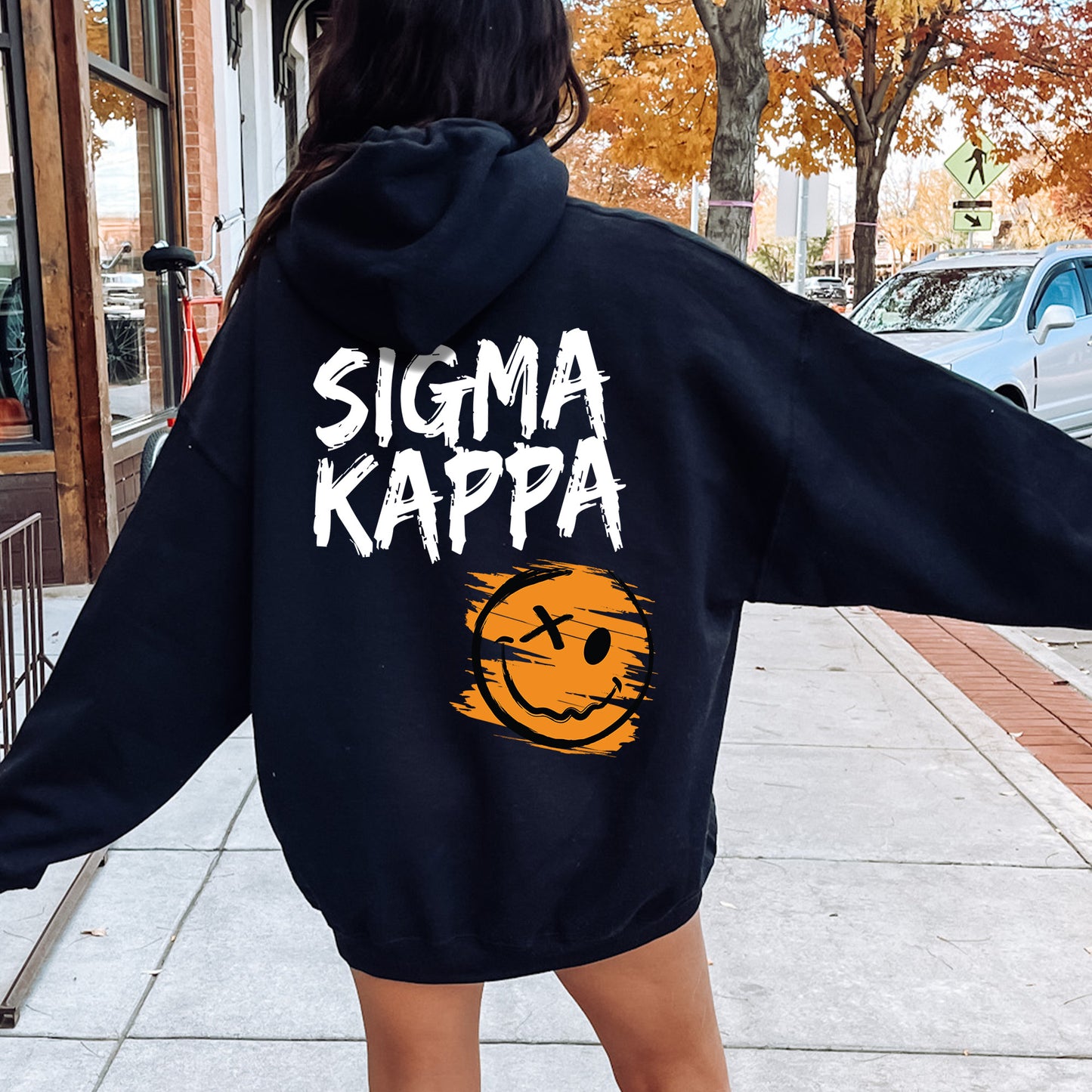 a woman walking down a sidewalk wearing a black hoodie